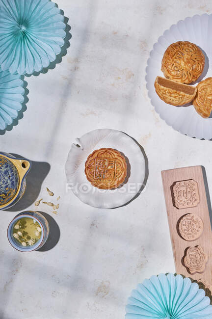 Desde arriba de tortas de luna tradicionales con relleno servido en la mesa con moldes para hornear cerca de hervidor de agua con té de hierbas en la sala de luz - foto de stock