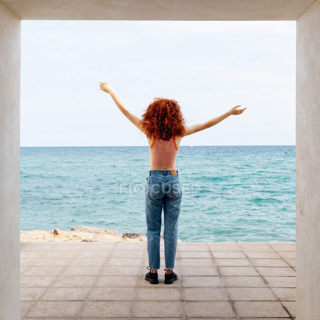 Back view full length of unrecognizable female tourist with outstretch arms admiring rippling sea from concrete passage on coast — Stock Photo