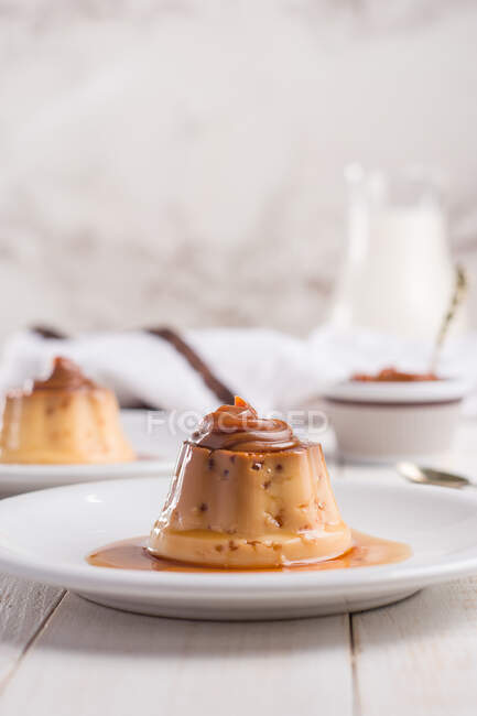 Egg custards topped with sweet Dulce de leche served on white plates on table with cutlery in kitchen — Stock Photo
