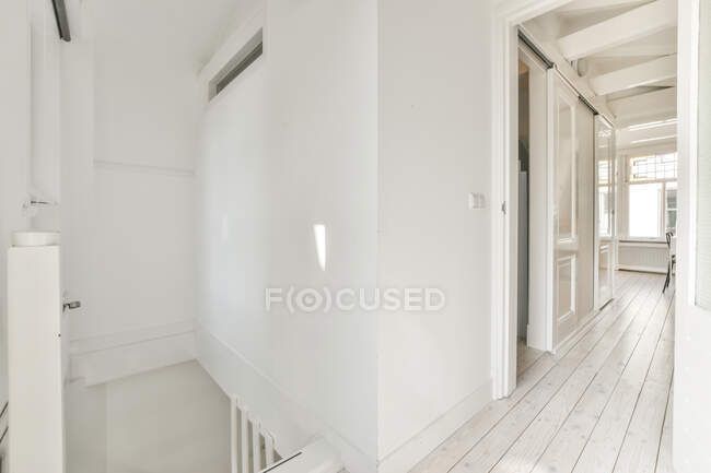 Intérieur minimaliste du couloir blanc contemporain avec escalier et portes dans un appartement lumineux spacieux en journée — Photo de stock