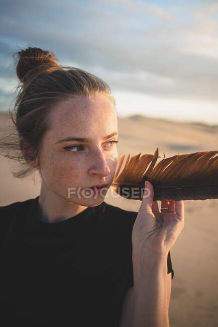 Серйозна жінка з чорним пір'ям на піщаній дюні, випрана морем після заходу сонця. — стокове фото