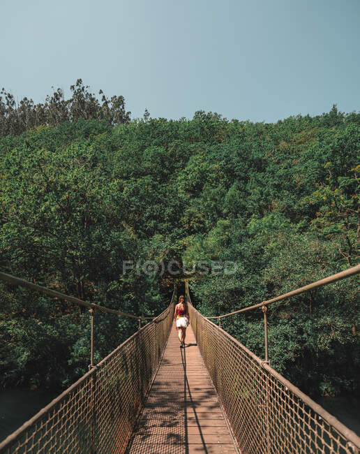 Rückansicht einer anonymen Forscherin, die an einem sonnigen Tag in Spanien auf einer Metallhängebrücke im Naturpark Fragas do Eume steht — Stockfoto