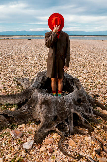 Pessoa irreconhecível em chapéu vermelho e casaco em pé no centro do toco na costa com pedras esmagadas no verão — Fotografia de Stock
