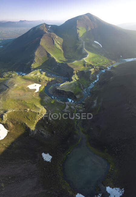 Узкий ручей, протекающий по горной местности, покрытой зеленой травой в высокогорье Исландии, против голубого неба в солнечный день — стоковое фото