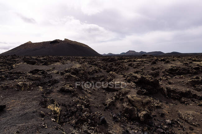 Scenery view of volcano Cuervo and rough mounts under cloudy sky in Tinajo Lanzarote Canary Islands Spain — Stock Photo