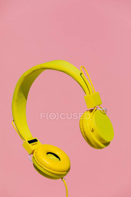 Auriculares inalámbricos modernos amarillos para escuchar música colgando en el aire sobre un fondo rosa brillante - foto de stock