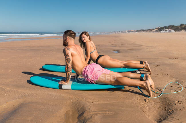 Ganzkörper-Seitenansicht von Sportlern in Badebekleidung, die auf Surfbrettern liegen, während sie sich auf das Surfen am Sandstrand im tropischen Badeort vorbereiten — Stockfoto