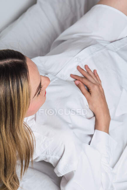 Dall'alto giovane femmina incinta gentile che tocca la pancia mentre si sdraia sul letto — Foto stock