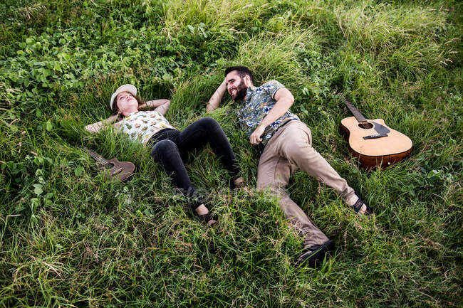 Músicos amigos felizes com guitarra e ukulele sentado na grama verde na costa perto do oceano na natureza durante o dia — Fotografia de Stock