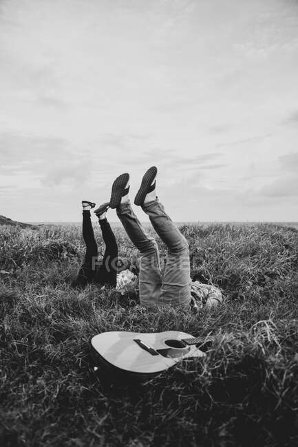 Schwarz-Weiß-Seitenansicht von fröhlichen Freunden in lässiger Kleidung, die mit erhobenen Beinen auf einer Wiese in der Natur bei Tageslicht liegen — Stockfoto