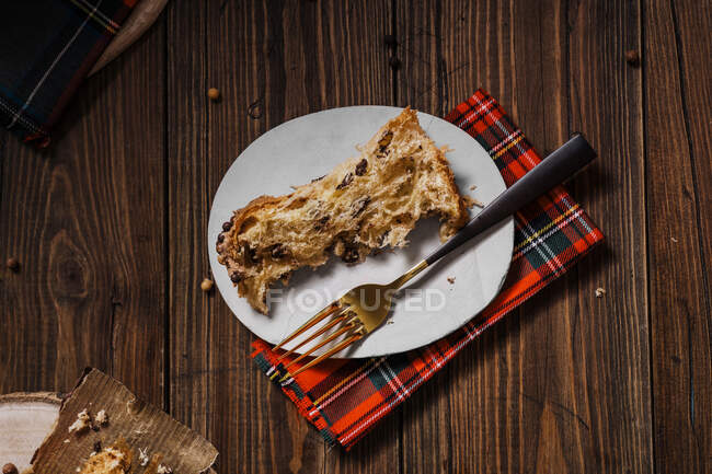 From above of delicious homemade baked Italian Panettone on plate near fork served on checkered napkin for Christmas — Stock Photo