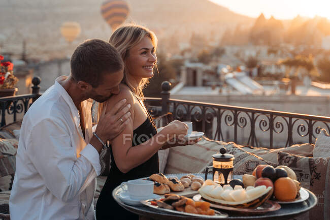 Vista lateral do amor masculino beijando ombro da esposa enquanto comem sobremesa e bebem chá juntos no terraço — Fotografia de Stock