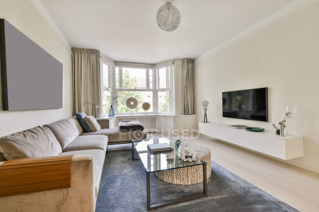 Удобный диван, расположенный под чистым полотном рядом со стеклянным столом и стулом в светлой элегантной гостиной — стоковое фото