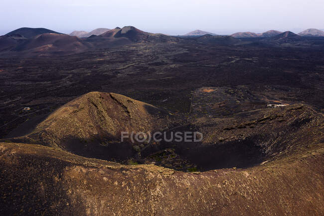 Scenery view of vineyard in crater of volcano against dry mounts under light sky in Geria Lanzarote Canary Islands Spain — Stock Photo