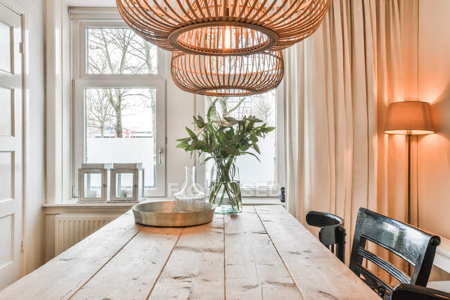 Diseño creativo de comedor con ramitas de plantas en jarrón sobre mesa de madera bajo lámparas en casa de luz - foto de stock