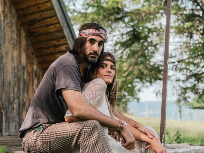 Attractive hippie couple embracing on the porch steps in front of the cabin — Stock Photo