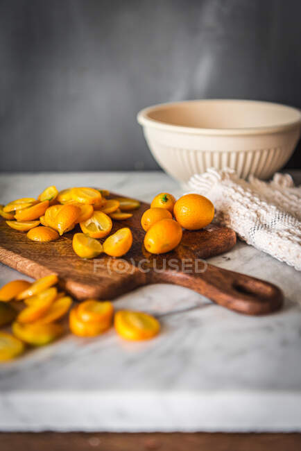 Haufen frischer, orange geschnittener Kumquats auf einem hölzernen Schneidebrett auf einem Marmortisch mit Handtuch in der Küche — Stockfoto