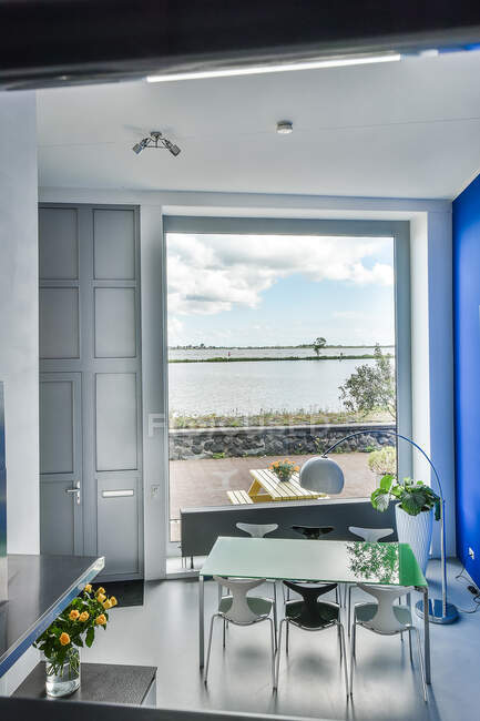Modernes Esszimmerinterieur mit Stühlen und Tisch unter Lampe gegen Fensterwand und Wohnungstür — Stockfoto