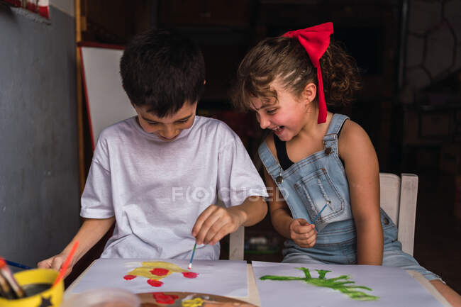 Позитивні діти з фарбувальними пензлями з барвистими акварелями на папері за столом — стокове фото