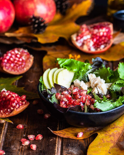 Insalata di melograno appetitosa in ciotola recisa su tavolo di legno con foglie autunnali su fondo nero — Foto stock