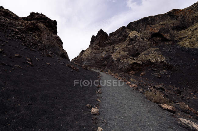 Scenery view of bath between volcano Cuervo and rough mounts under cloudy sky in Tinajo Lanzarote Canary Islands Spain — Stock Photo