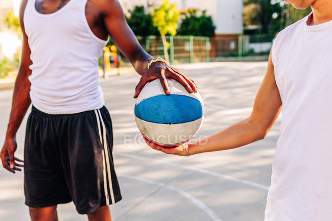 Colheita anônima afro-americano jogadores do sexo masculino de pé com bola em campo de esportes de basquete no verão — Fotografia de Stock