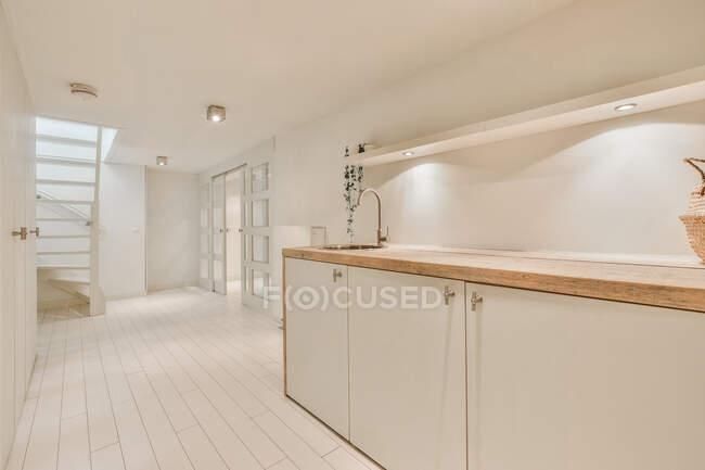 Interior de la cocina contemporánea con lavabo y mesa contra escaleras y puertas en casa con lámparas - foto de stock