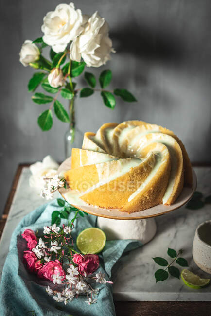 Смачний пиріг з губкою, поданий на білій тарілці поблизу квітів та скибочок лайма — стокове фото
