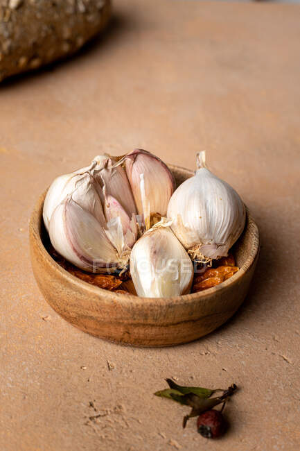 Spicchi d'aglio non pelati con buccia bianca serviti in piccola ciotola rotonda di legno posta sul tavolo marrone in cucina leggera — Foto stock