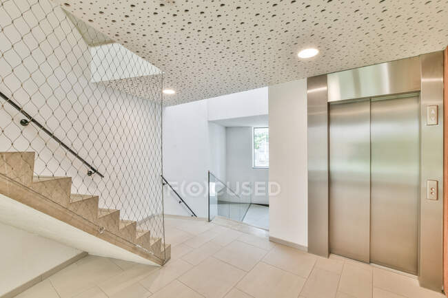 Интерьер просторного коридора нового жилого дома с лифтом и встроенными лампочками на потолке — стоковое фото