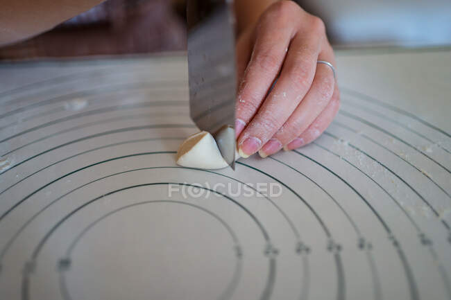 High angle of crop anonymous lady cutting raw dough with putty knife while preparing homemade dumplings sitting at table in kitchen — Stock Photo