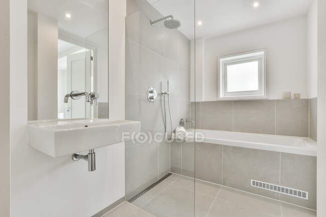 Lavatório branco e espelho instalado na parede perto da cabine do chuveiro com banheira no banheiro moderno — Fotografia de Stock