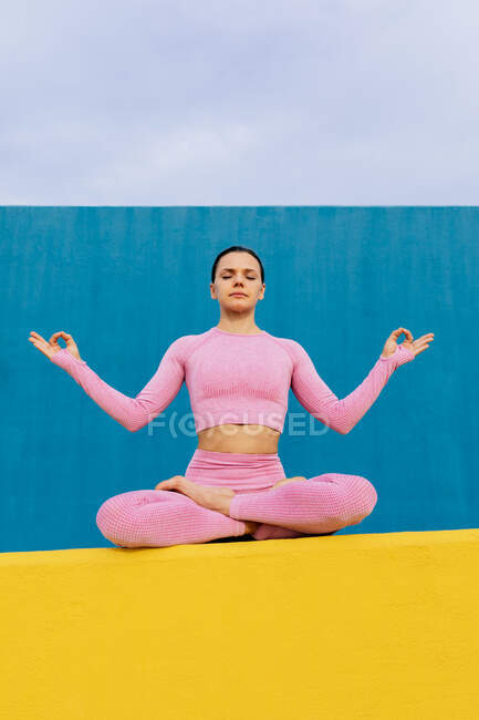 Von unten eine junge Frau in aktiver Kleidung, die in Lotus-Pose auf einem Sportplatz sitzt und meditiert — Stockfoto