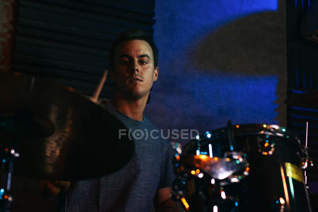 Концентрований молодий чоловічий музикант грає на барабанах у клубі з зеленим і синім неоновим освітленням — стокове фото