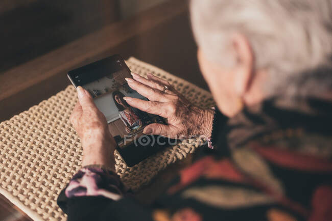 Dall'alto le donne anziane allargano e ispezionano l'immagine della giovane nipote su tablet mentre si siede a tavola a casa. — Foto stock