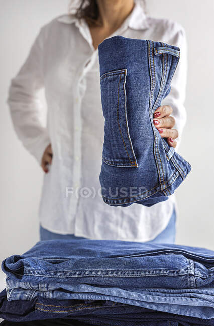 Анонимная женщина в белой рубашке с пачкой синих джинсов в руках — стоковое фото