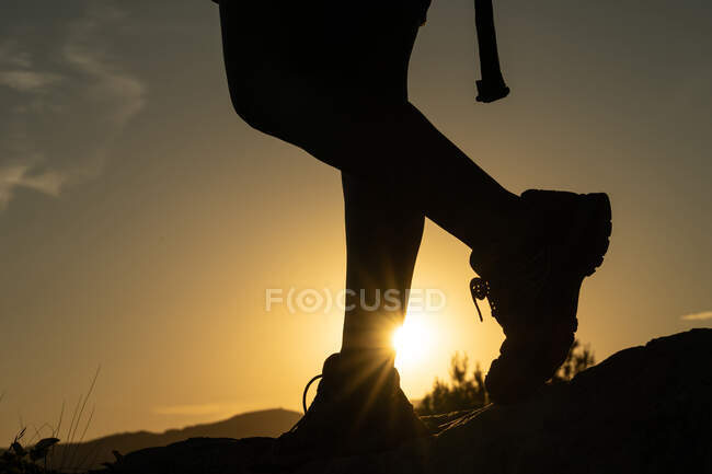 Silueta de las piernas de una mujer haciendo trekking en la montaña con el sol creando una estrella solar con su pie al atardecer - foto de stock