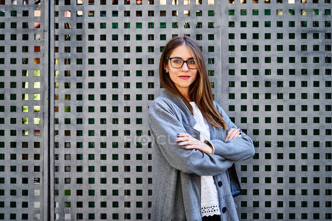 Well dressed female employee standing near metal fencing and looking at camera with smile — Stock Photo