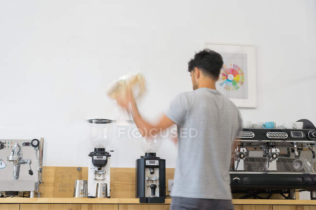 Visão traseira do barista masculino anônimo derramando grãos de café do saco no moedor de café profissional moderno no balcão de madeira na casa de café — Fotografia de Stock