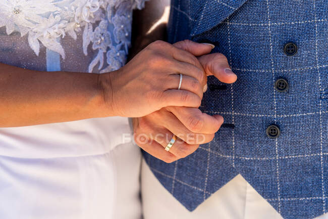 Crop faceless married couple in wedding outfits holding hands with wedding rings in daylight — Stock Photo