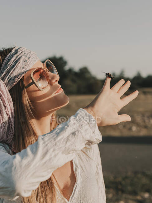 Side view of peaceful female hippie in sunglasses covering face from sunshine while spending time in nature on summer day — Stock Photo