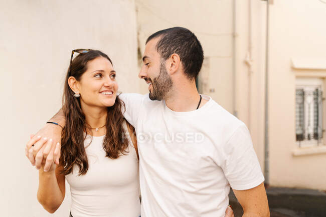 Cheerful enamored young Hispanic couple in casual clothes laughing while they walk down the street on city — Stock Photo