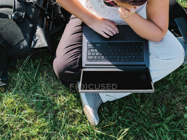 From above of crop anonymous female sitting with crossed legs on grassy lawn and browsing netbook — Stock Photo