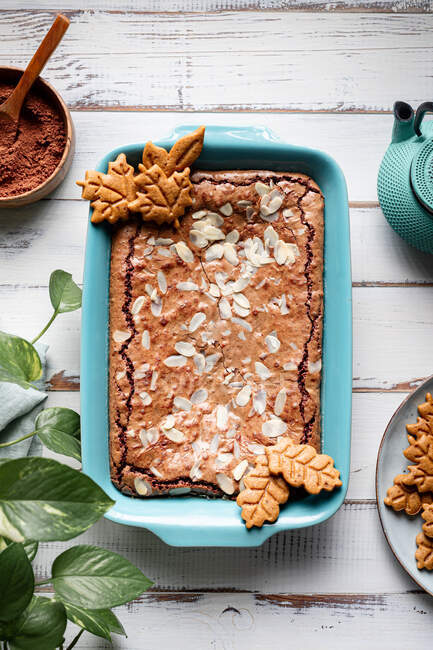 Draufsicht auf leckeren gebackenen Brownie mit Mandelflocken im Backblech mit Keksen auf Holztisch mit Kakaopulver platziert — Stockfoto