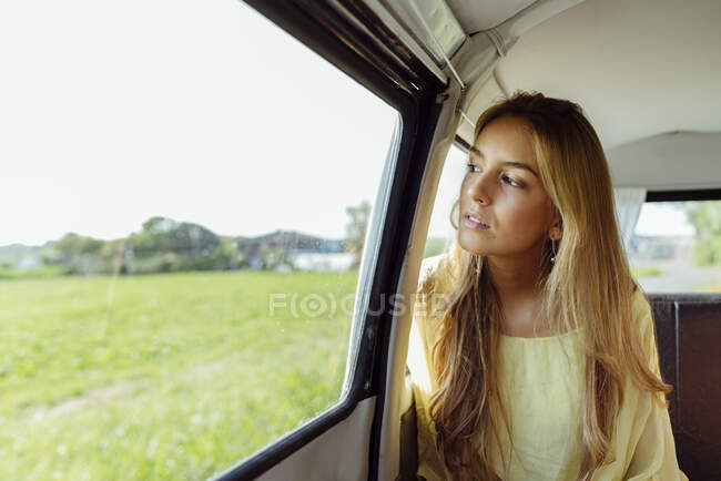 Linda chica rubia dentro de una furgoneta mirando por la ventana - foto de stock