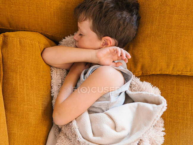 Вид зверху на хворого хлопчика, який лежить з закритими очима під ковдрою на дивані і спить у вітальні вдома — стокове фото