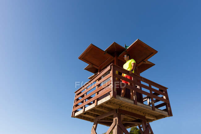 From below male lifeguard controlling safety on sea from wooden rescue tower — Stock Photo