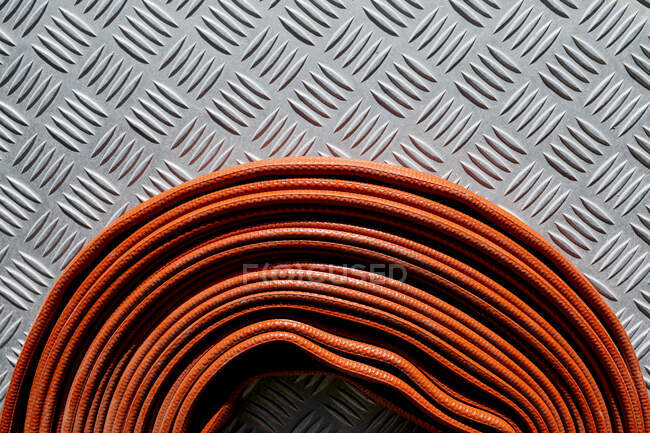 Rolled flexible red fire hose pinned to corrugated metal surface on daytime in bright sunlight — Stock Photo