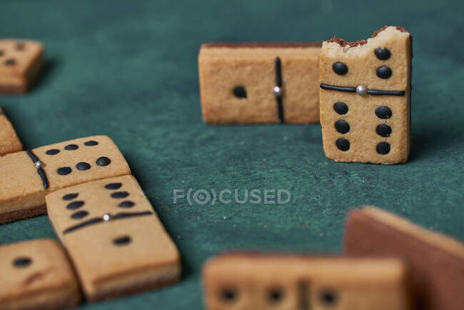 Un mucchio di dolci gustosi biscotti croccanti a forma di domino con punti neri e pezzo morso sparsi sulla superficie verde nella stanza della luce — Foto stock