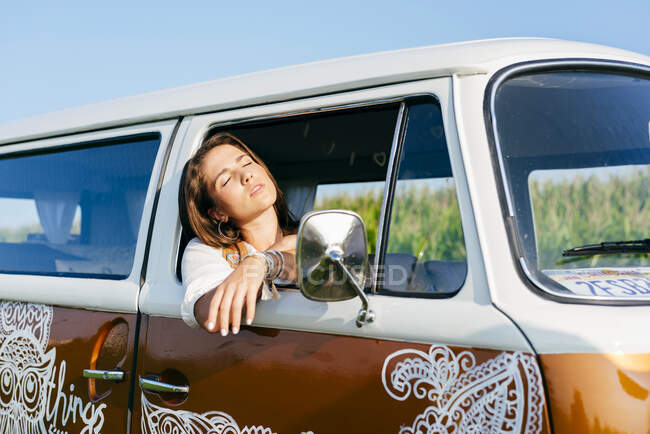 Beautiful brunette girl inside a van leaning on window and closing her eyes — Stock Photo